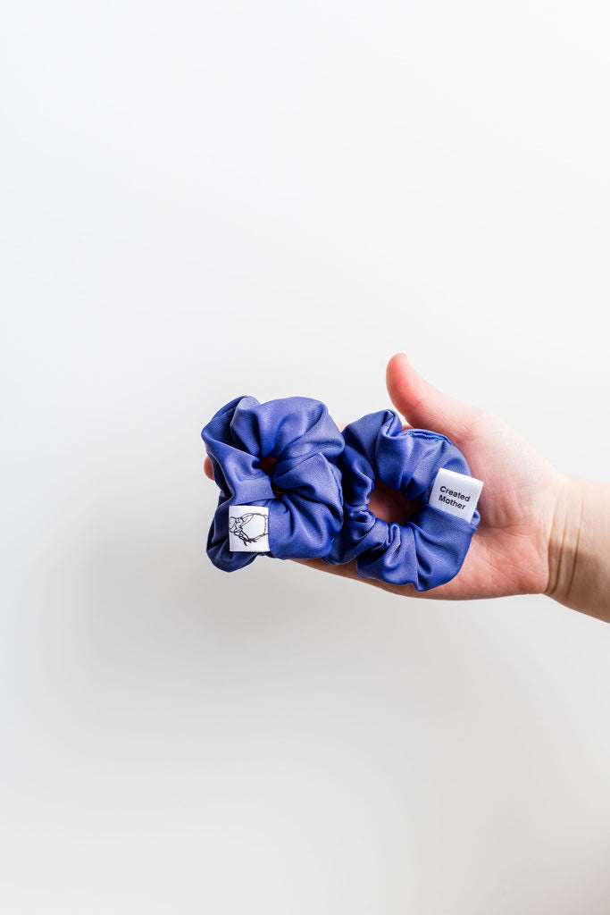 Hand holding two blue scrunchies with a white background