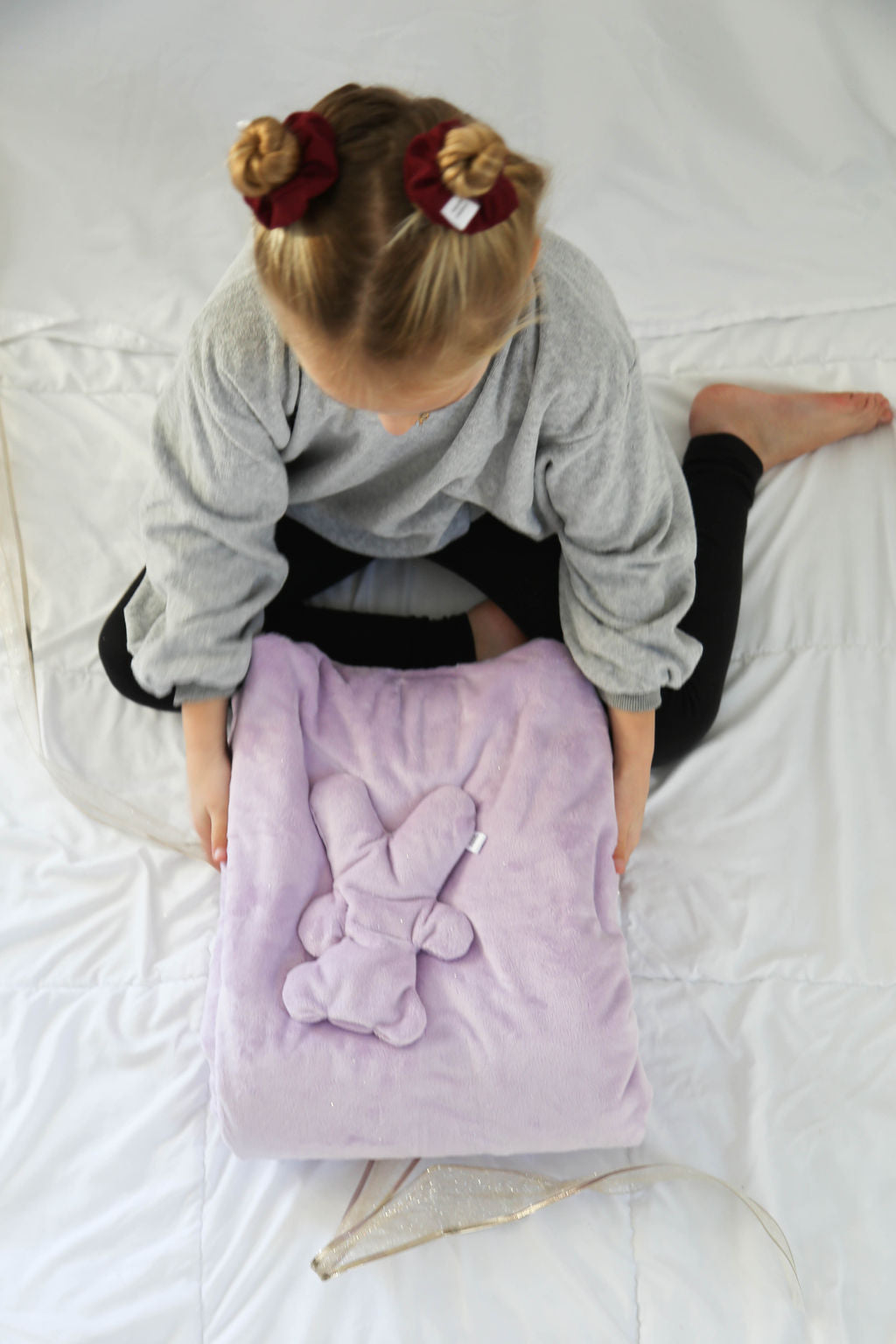 Child holding a purple blanket with a Hot/Cold Therapy Bear on a white bed.