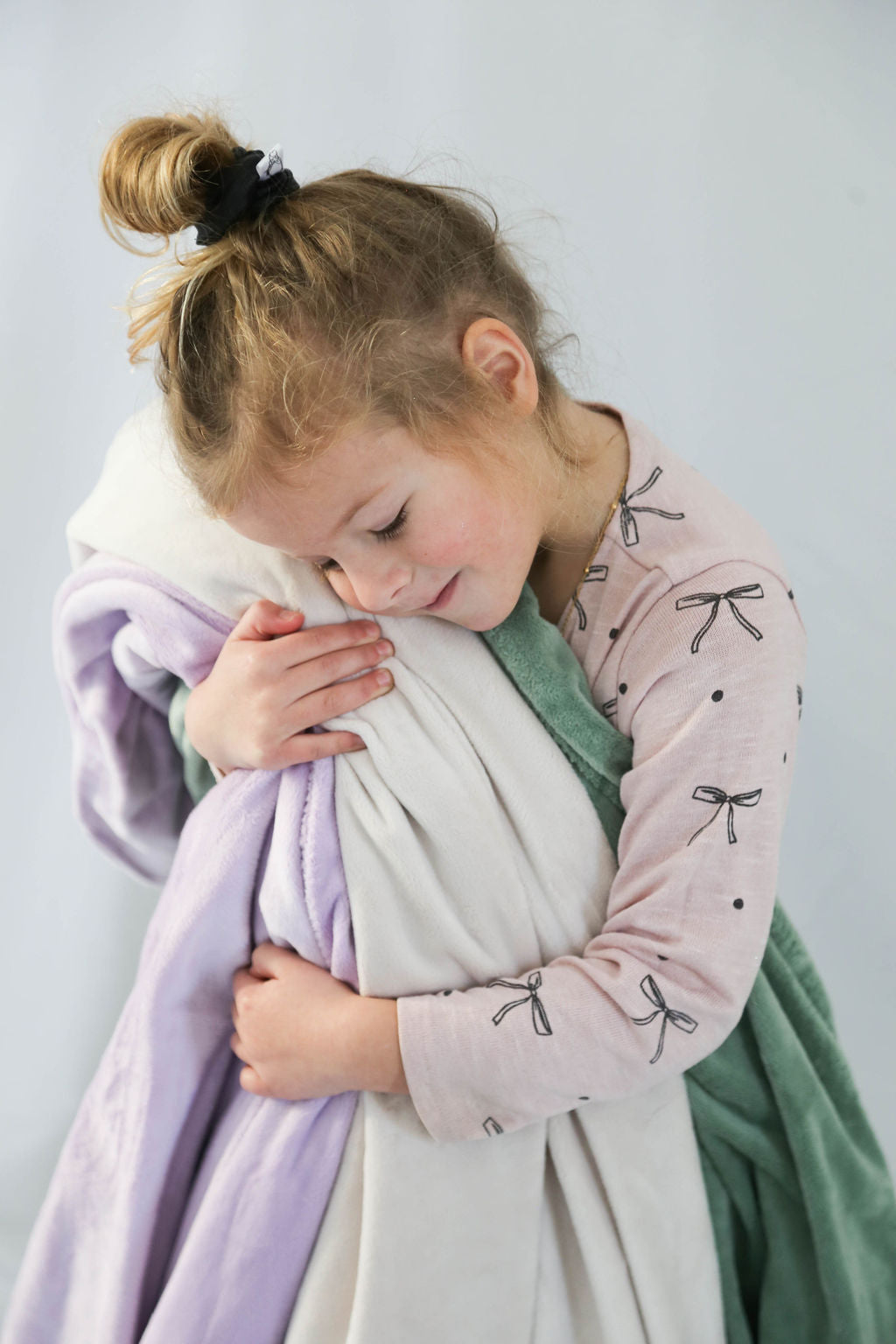 Child holding soft blankets against a light gray background