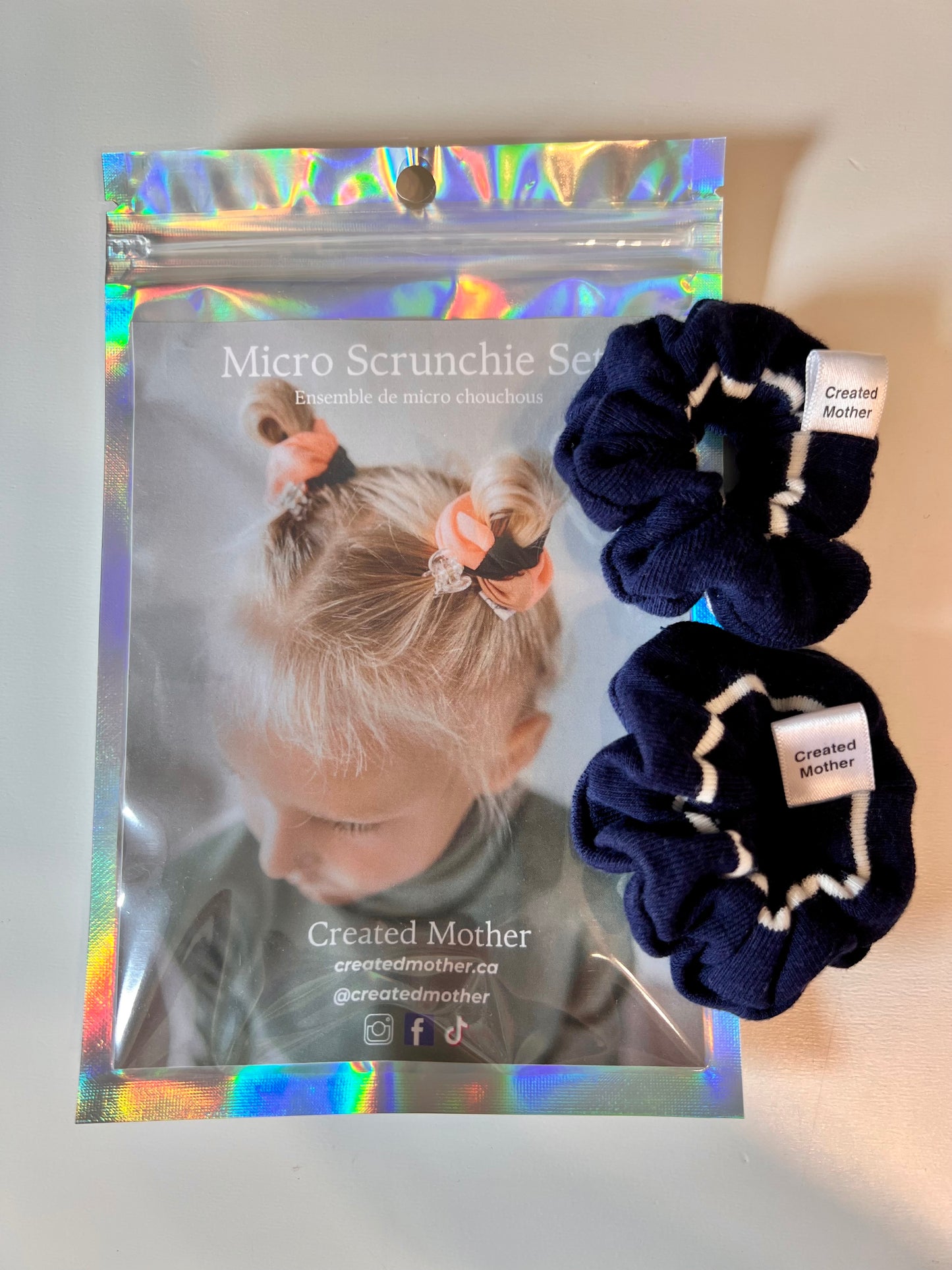 Navy blue scrunchies with white accents on a gray surface next to their packaging.
