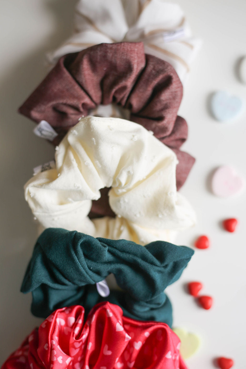 Set of colorful scrunchies on a light background with heart-shaped candies.