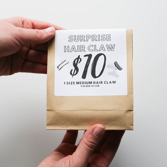 Hand holding a package with a label indicating a surprise hair claw product.