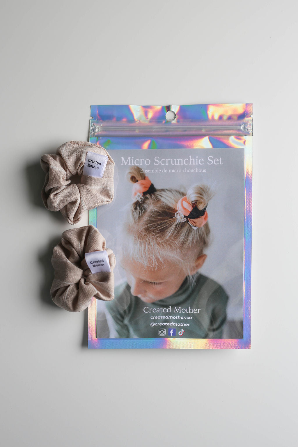 Two beige scrunchies next to their packaging featuring a child with hair accessories.