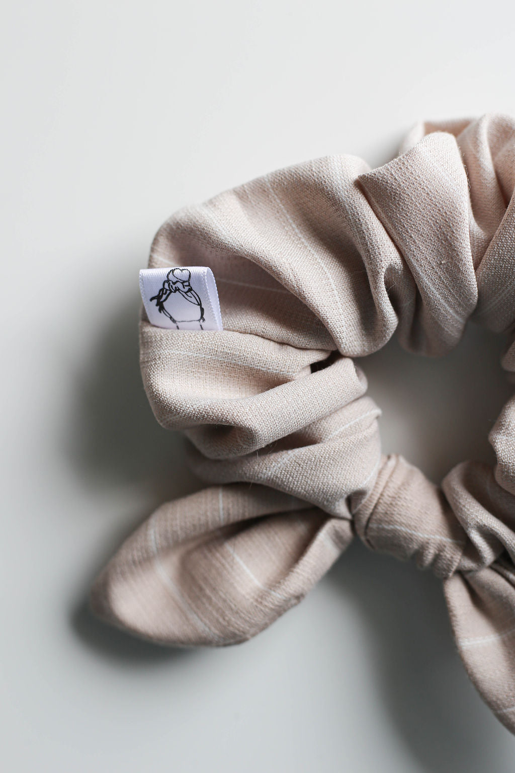 Beige bow scrunchie with a small label on a light gray background by Created Mother