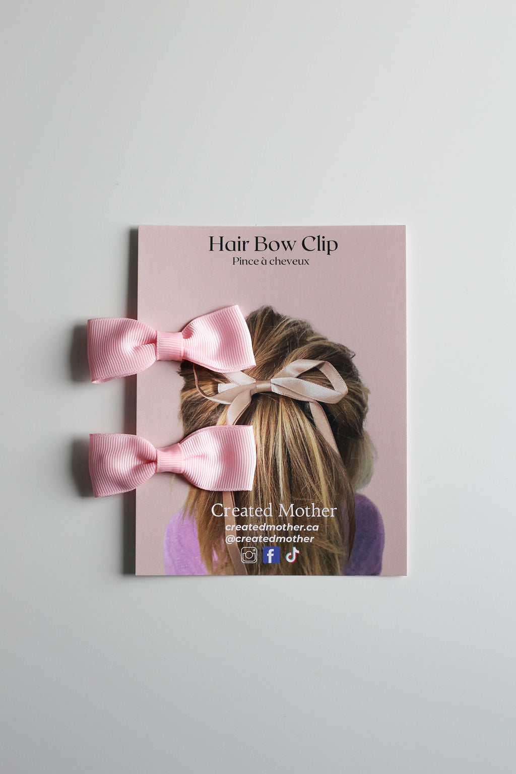 Set of two matching small bow alligator clips in soft pink, displayed on a branded card.