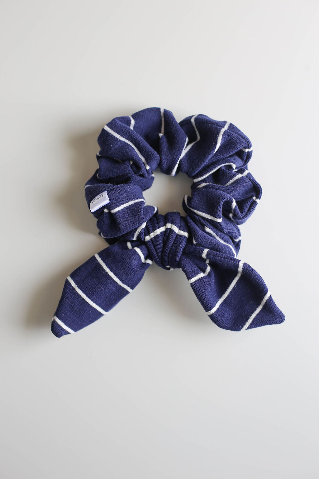 Navy blue scrunchie with white stripes on a light gray background