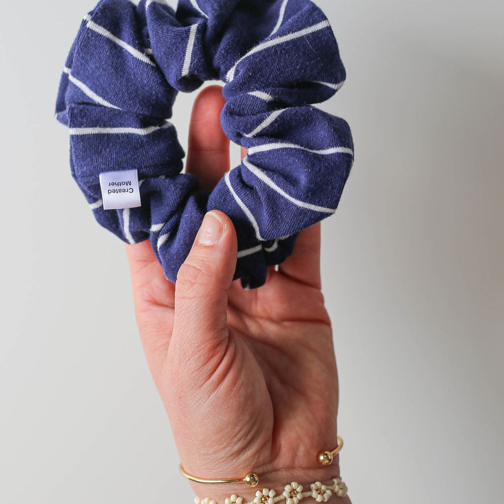 Navy blue scrunchie with white stripes held by a hand against a light gray background