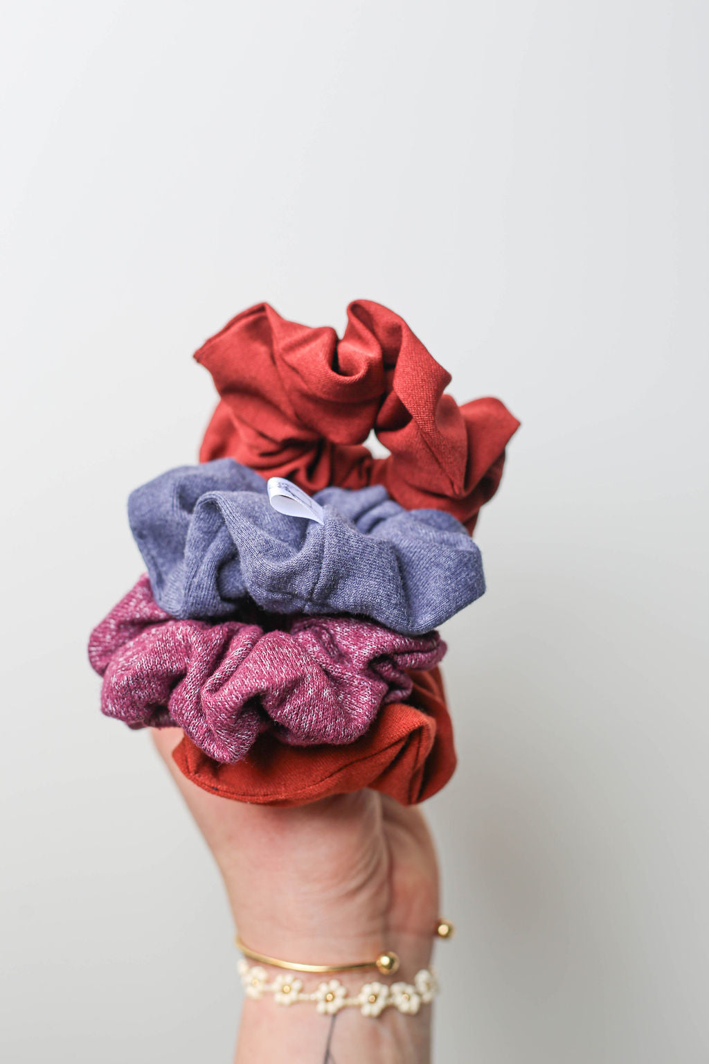 Three scrunchies in red, blue, and purple held by a hand against a light gray background