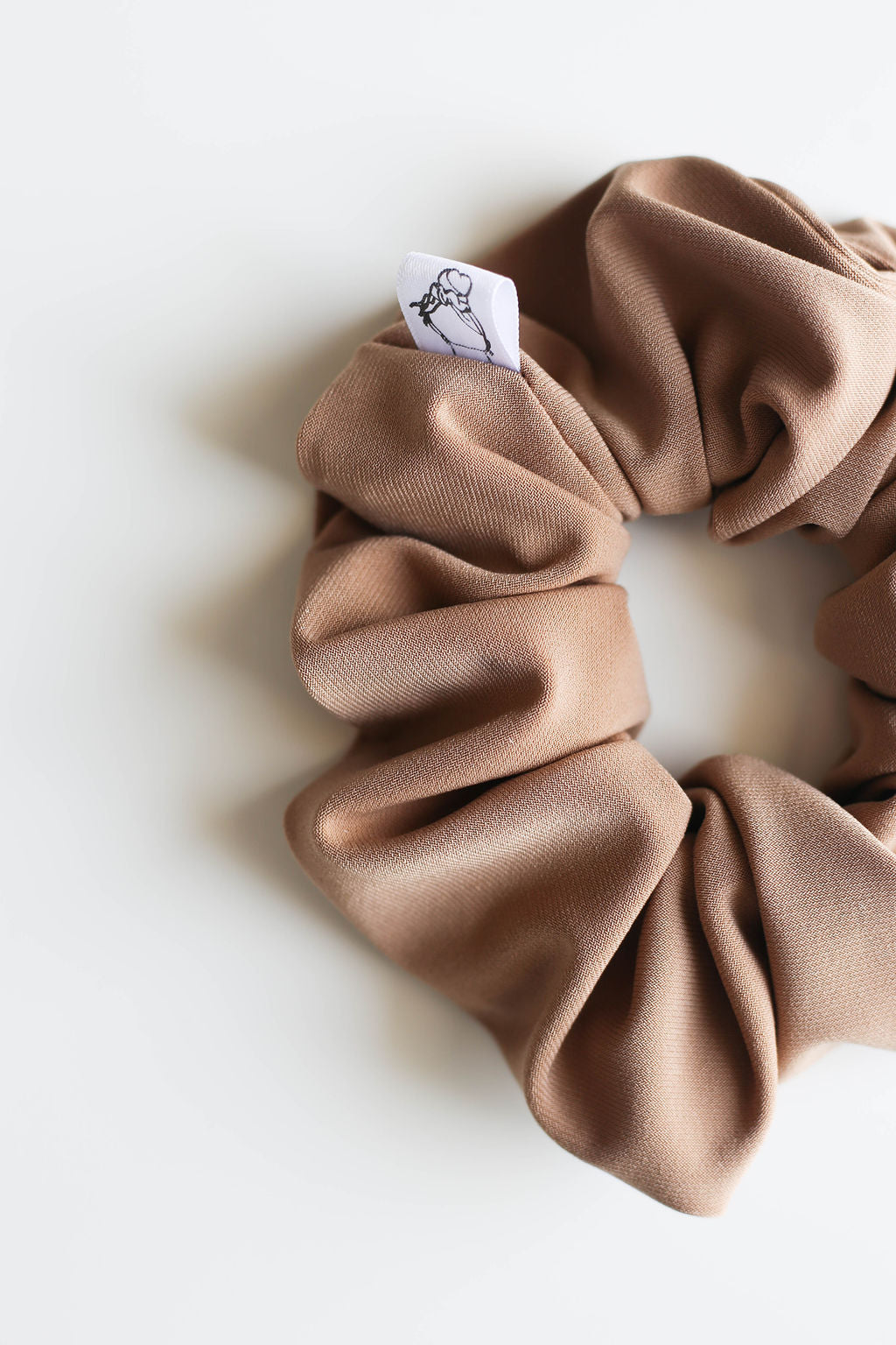 Brown scrunchie with a brand label on a white background