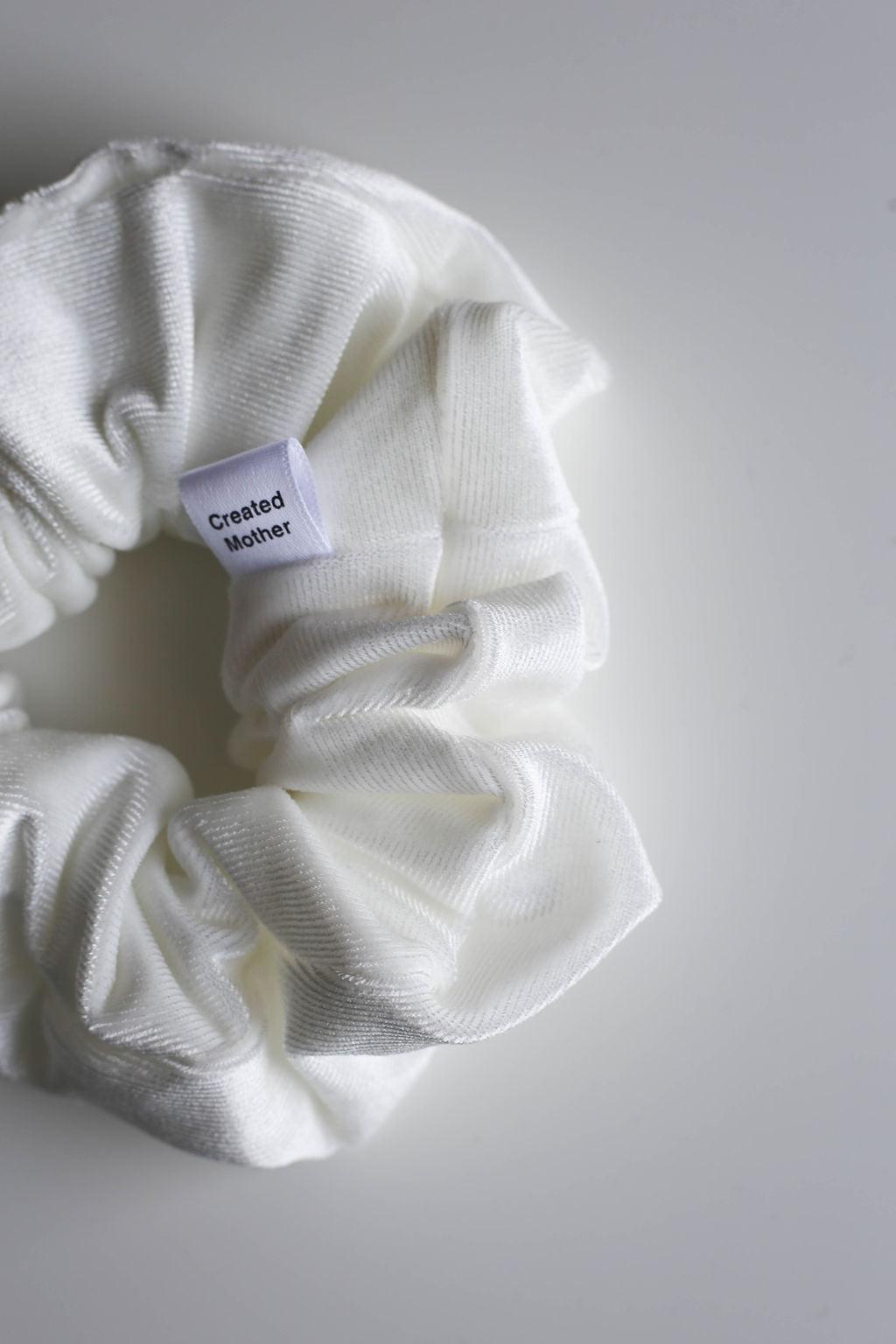 White velvet scrunchie with a label on a light gray background