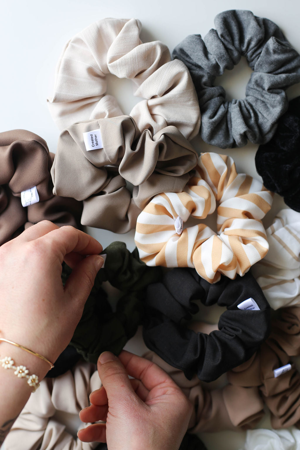 Collection of colorful scrunchies on a white surface with hands interacting with them.
