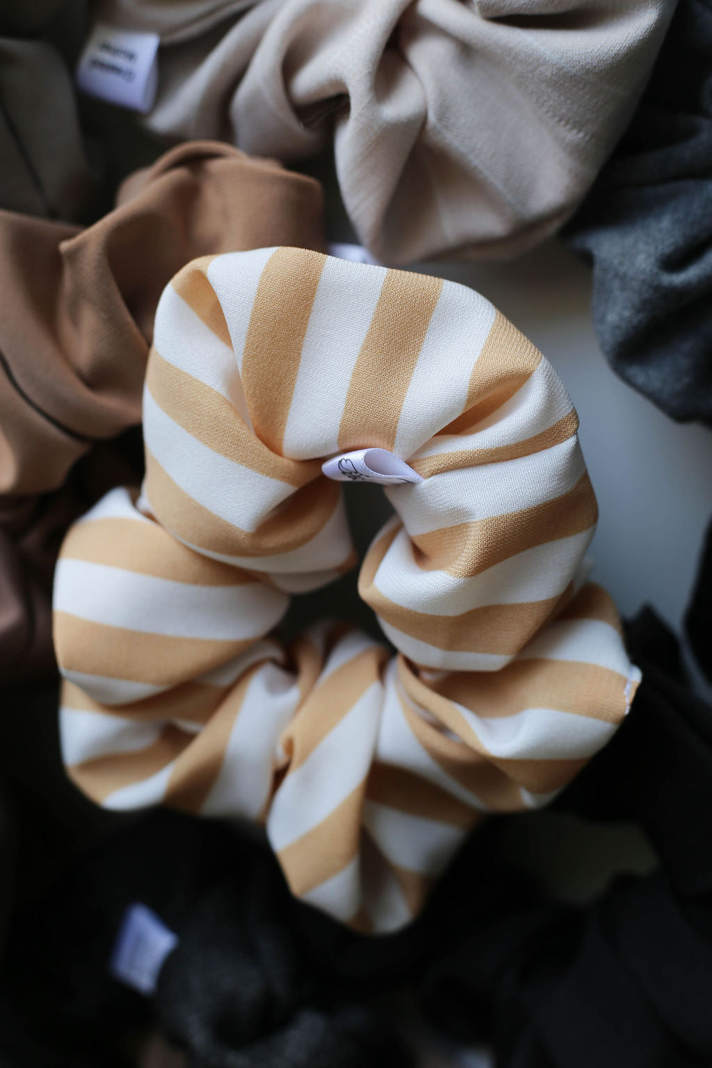 Striped scrunchie with beige and white stripes on a blurred fabric background