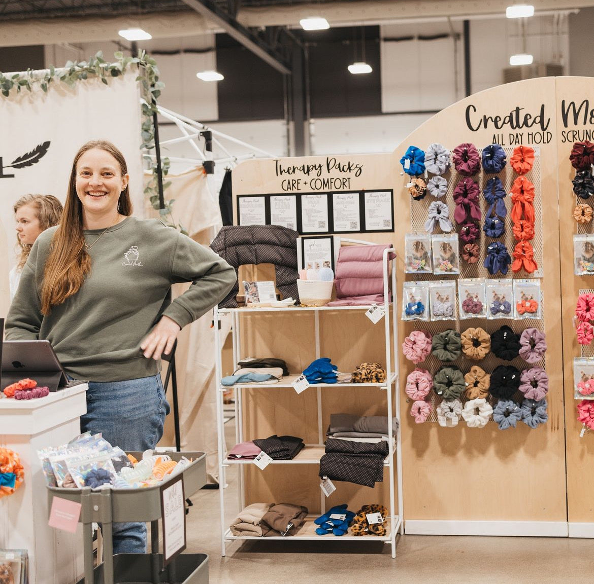 Woman standing in a store with a display of scrunchies and related products.