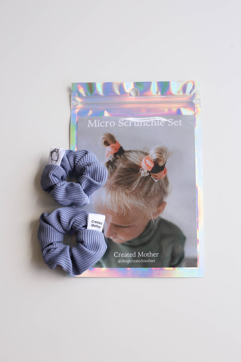 Two blue scrunchies with packaging featuring a child wearing them on a white background