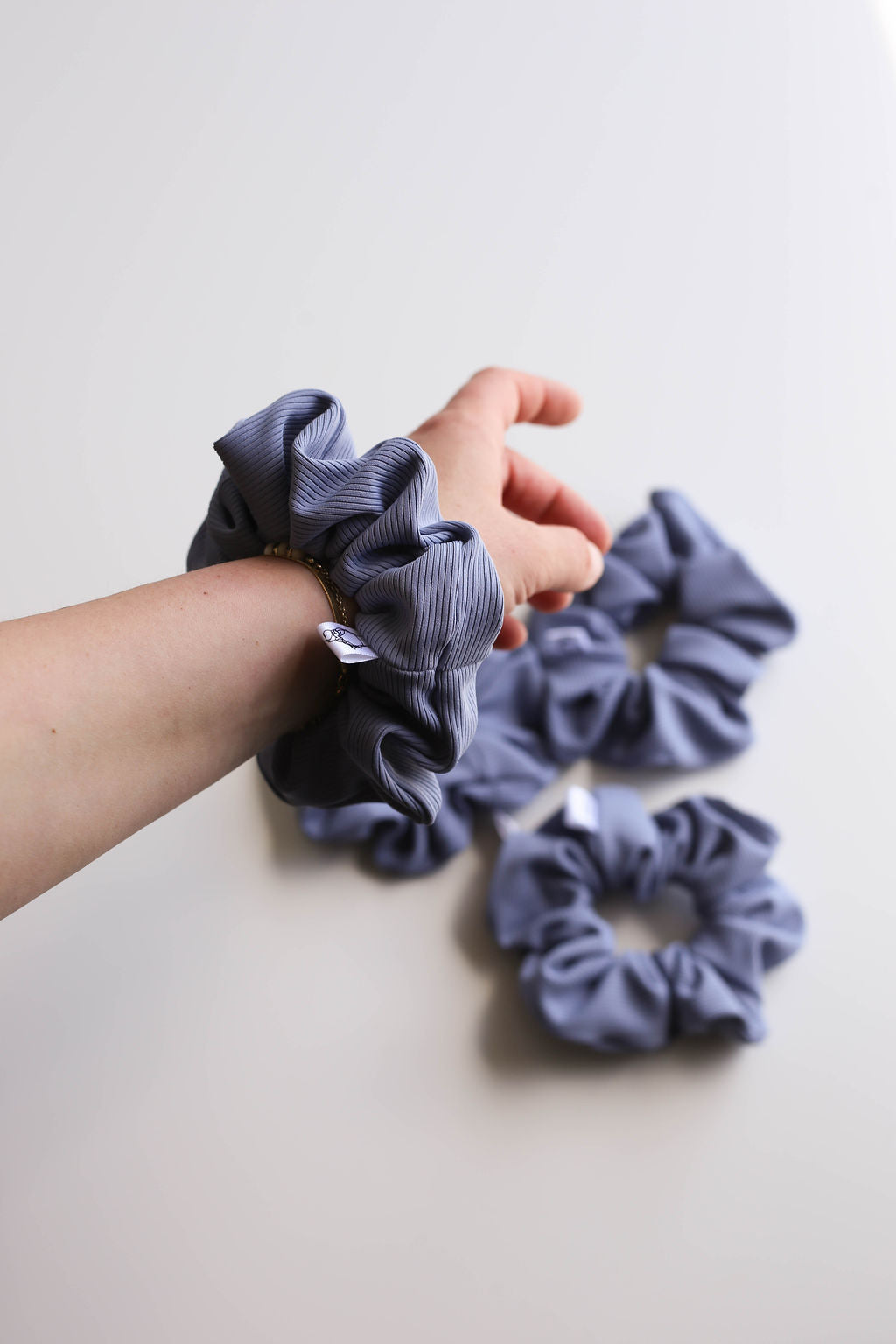 Hand holding a blue scrunchie with more scrunchies on a light background