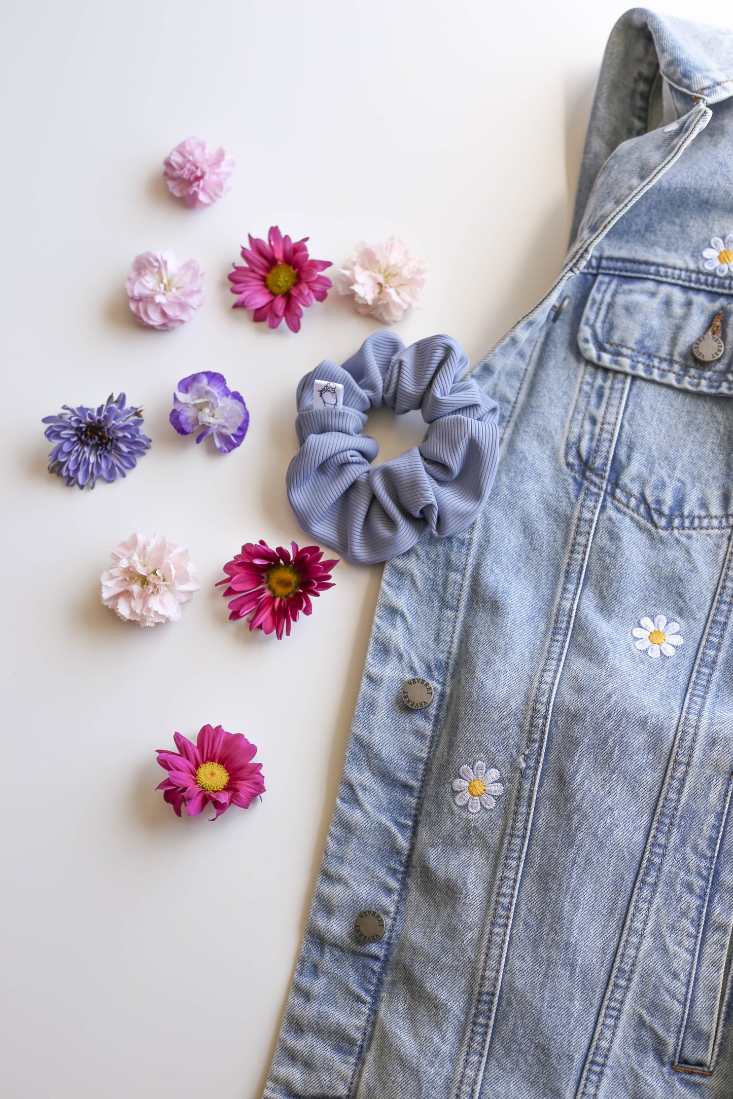 Blue SWIM Scrunchie with floral decorations next to flowers on a light background