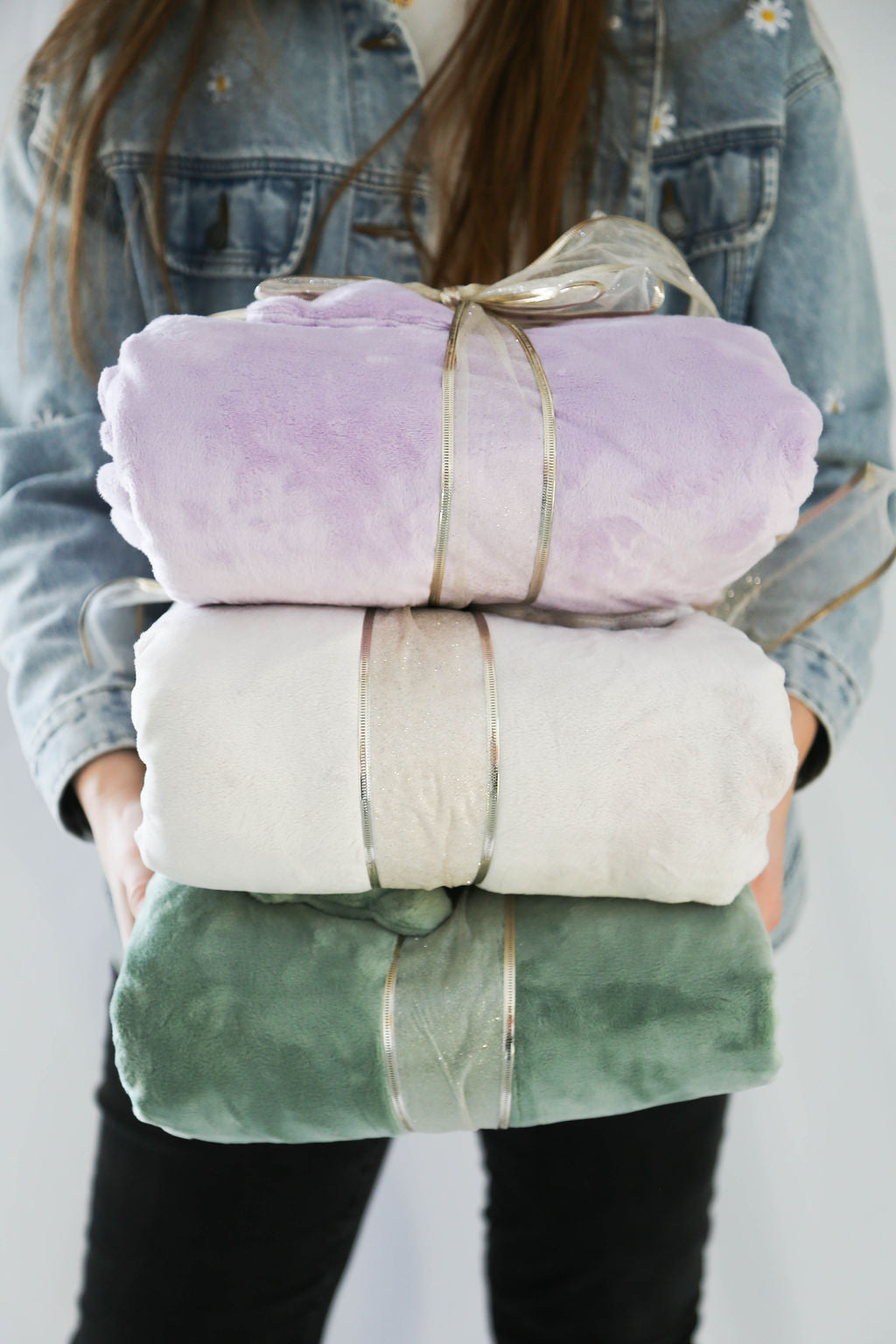 Person holding a stack of folded blankets in pastel colors against a neutral background