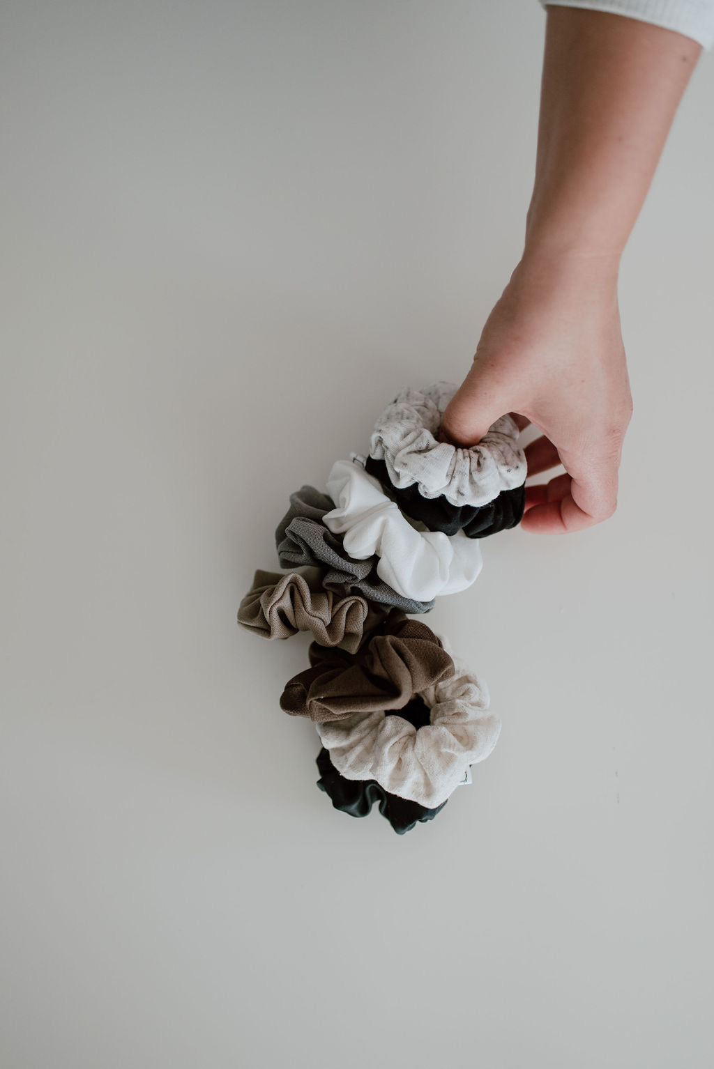 Hand holding a set of scrunchies against a plain background