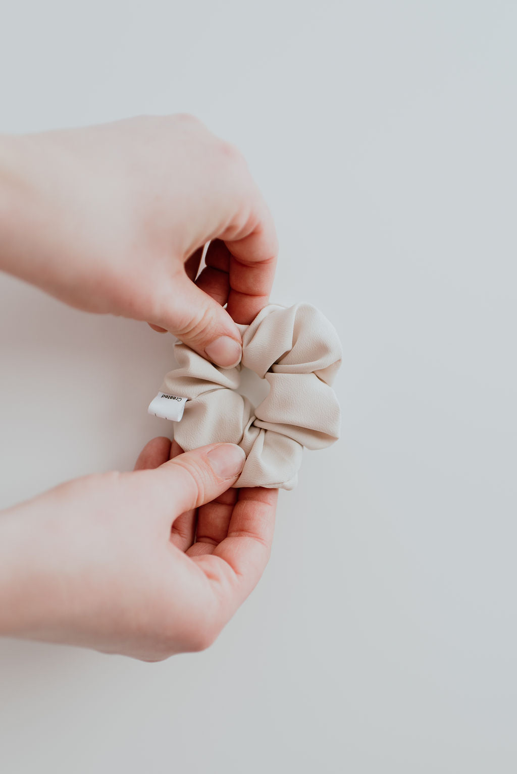Beige scrunchie held between two hands against a plain background