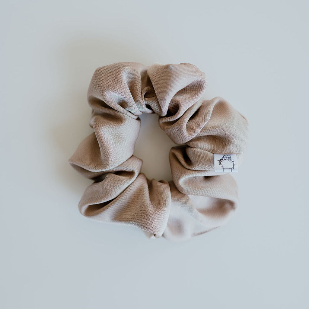Beige scrunchie with a brand label on a light gray background