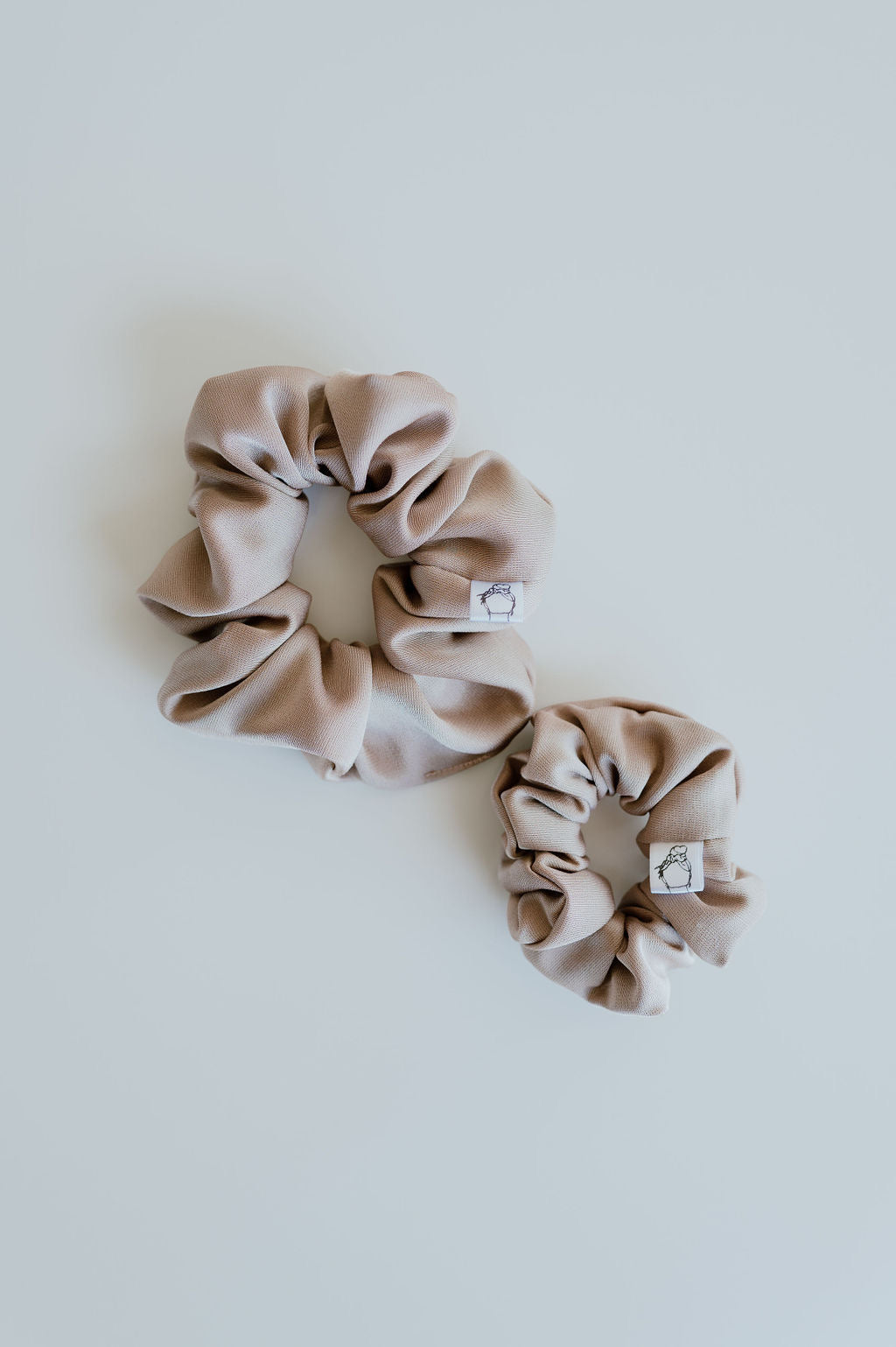 Two beige scrunchies on a white background