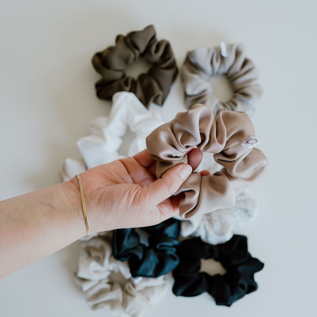 Hand holding a beige scrunchie with other scrunchies on a light background