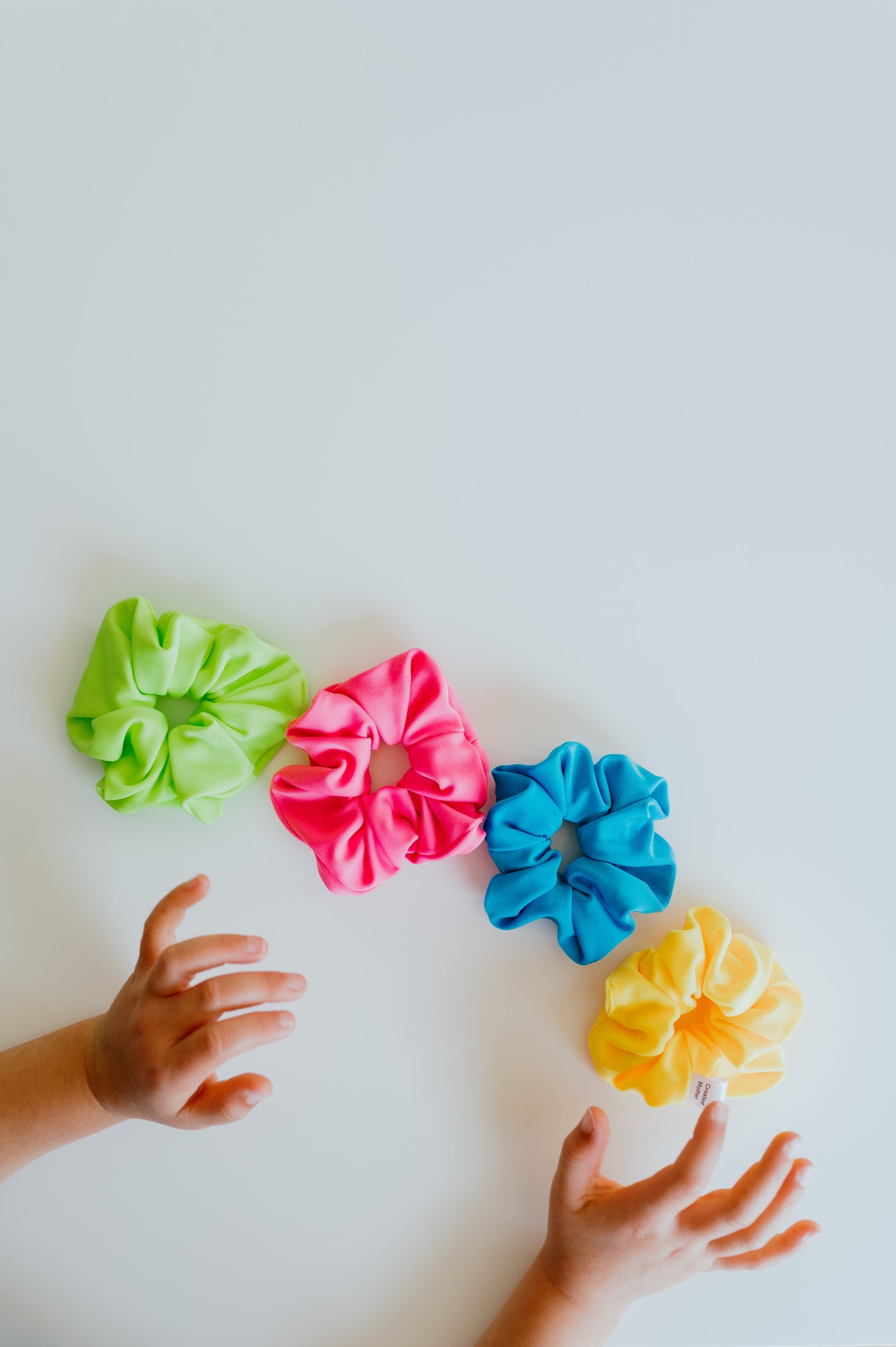 Colorful scrunchies on a white surface with child's hands reaching towards them.