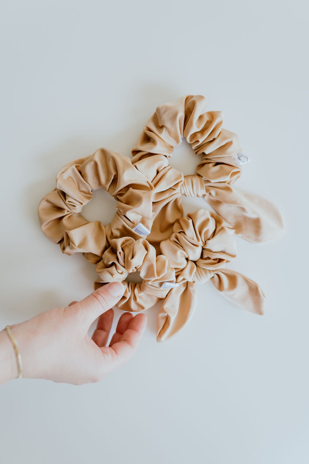 Beige scrunchies on a white background with a hand holding one scrunchie.