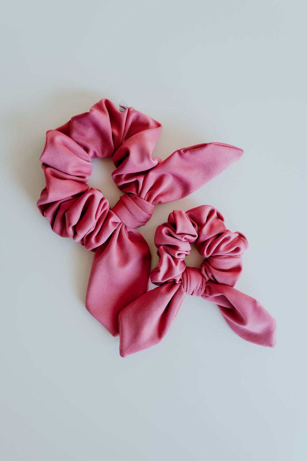 Two Coral pink SWIM scrunchies with bows on a light gray background