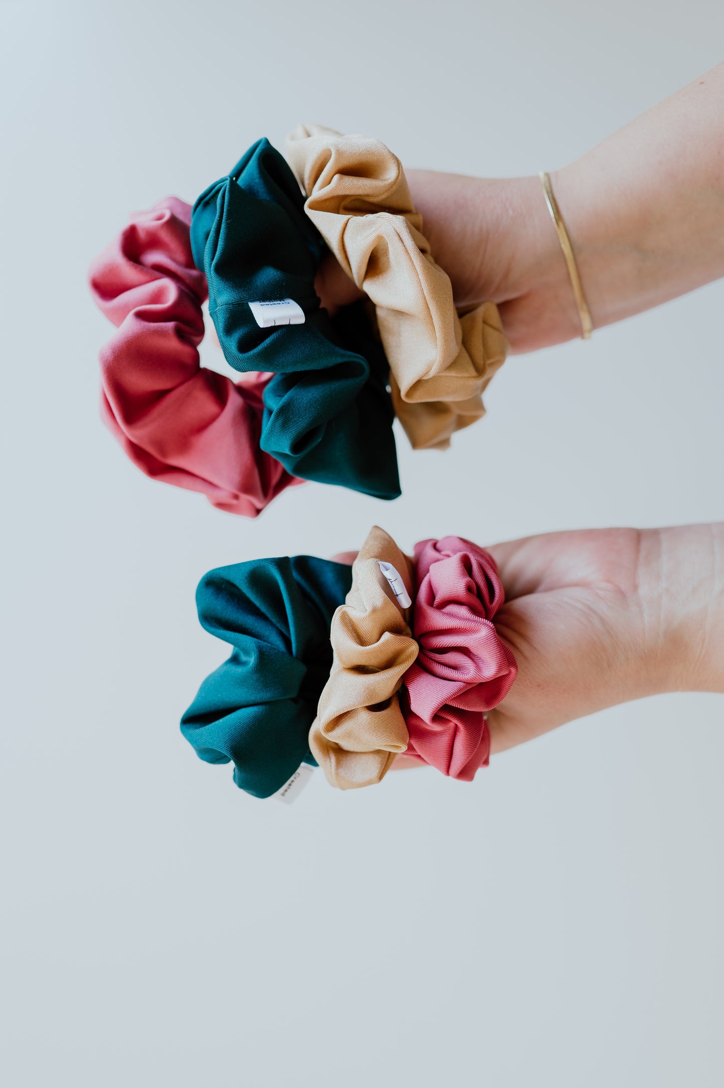 Two hands holding colorful SWIM scrunchies against a light background