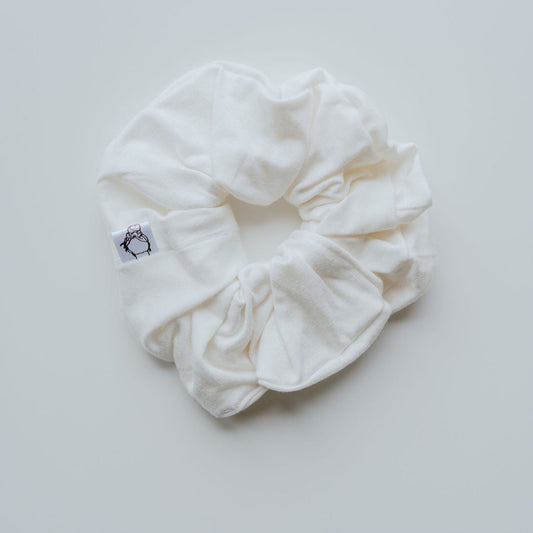 White scrunchie with a brand logo on a light gray background
