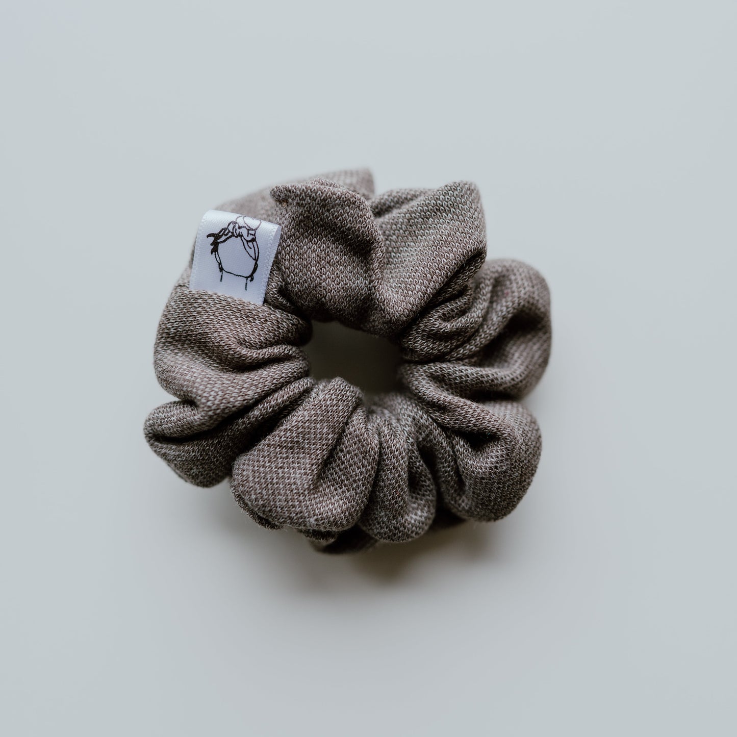 Gray scrunchie with a brand label on a light gray background