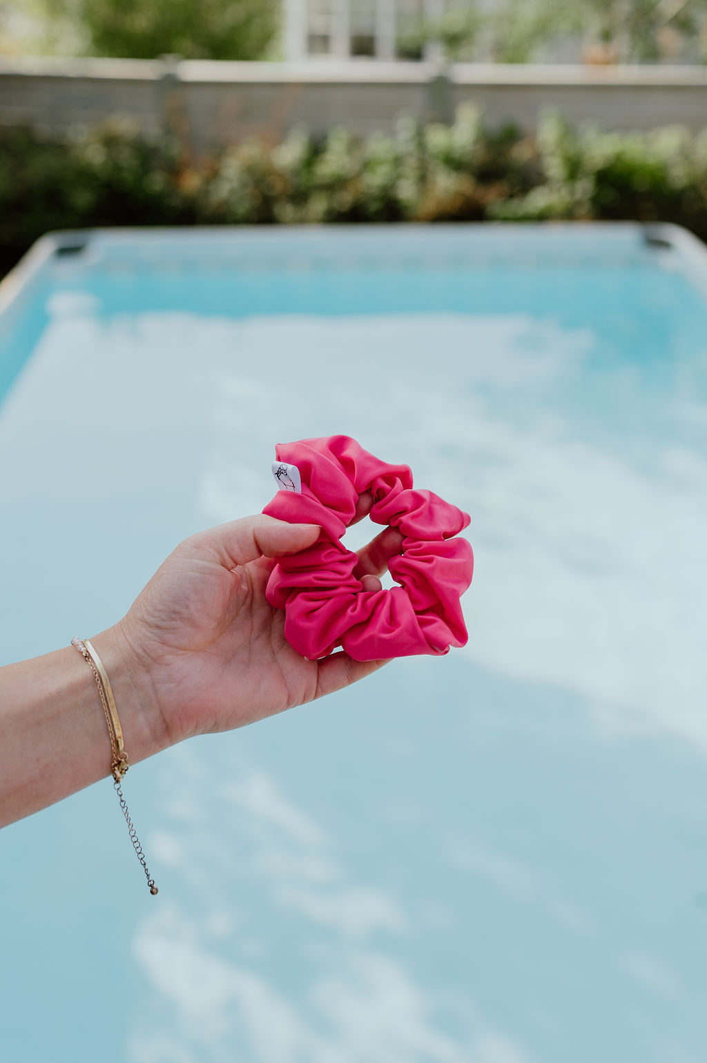Hand holding a pink scrunchie with a pool in the background