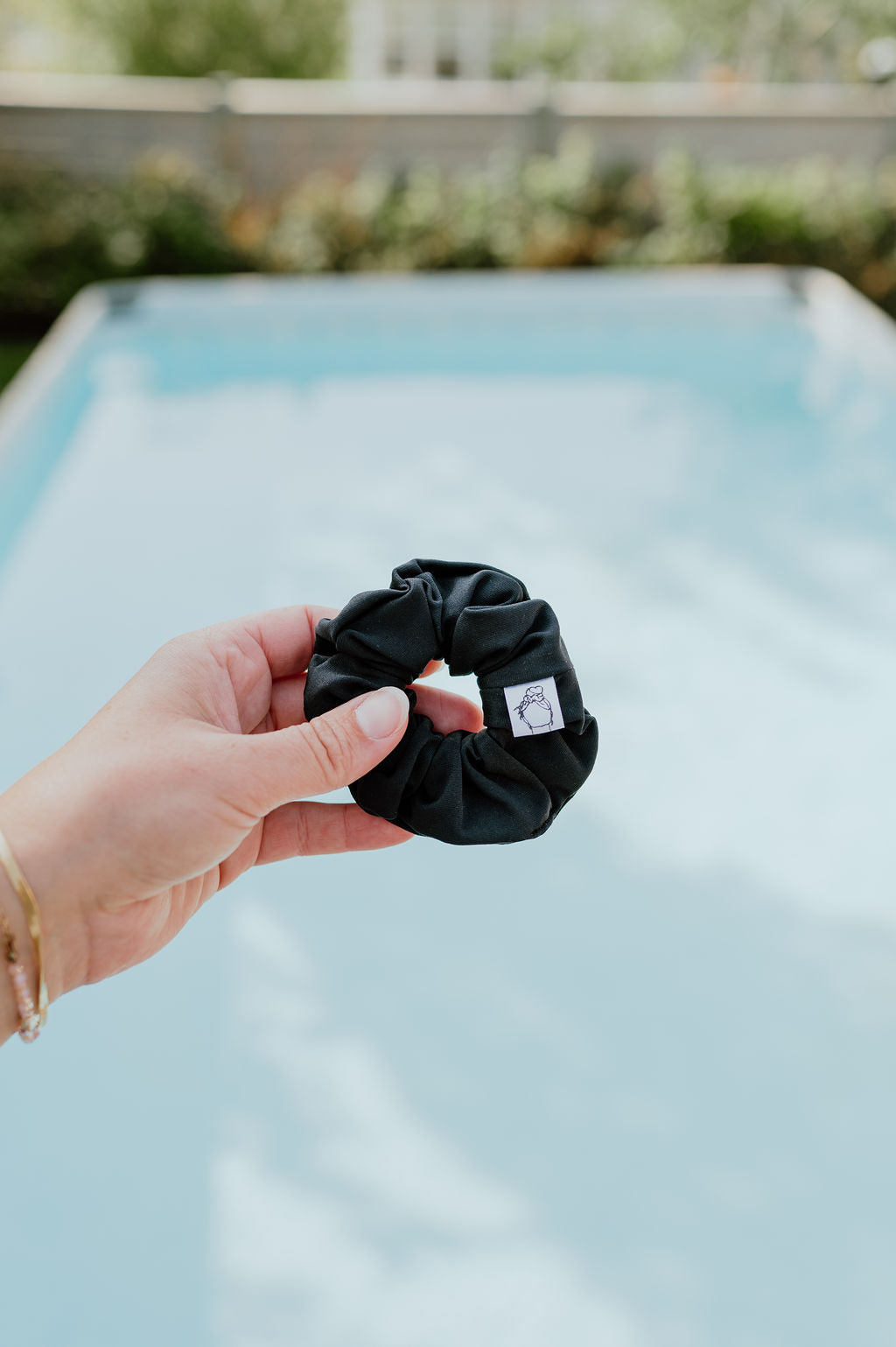 Black scrunchie held by a hand with a blurred pool background