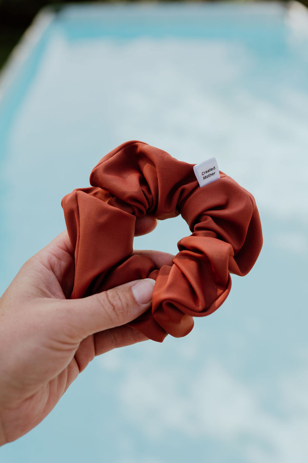 Hand holding a rust-colored scrunchie with a blurred background