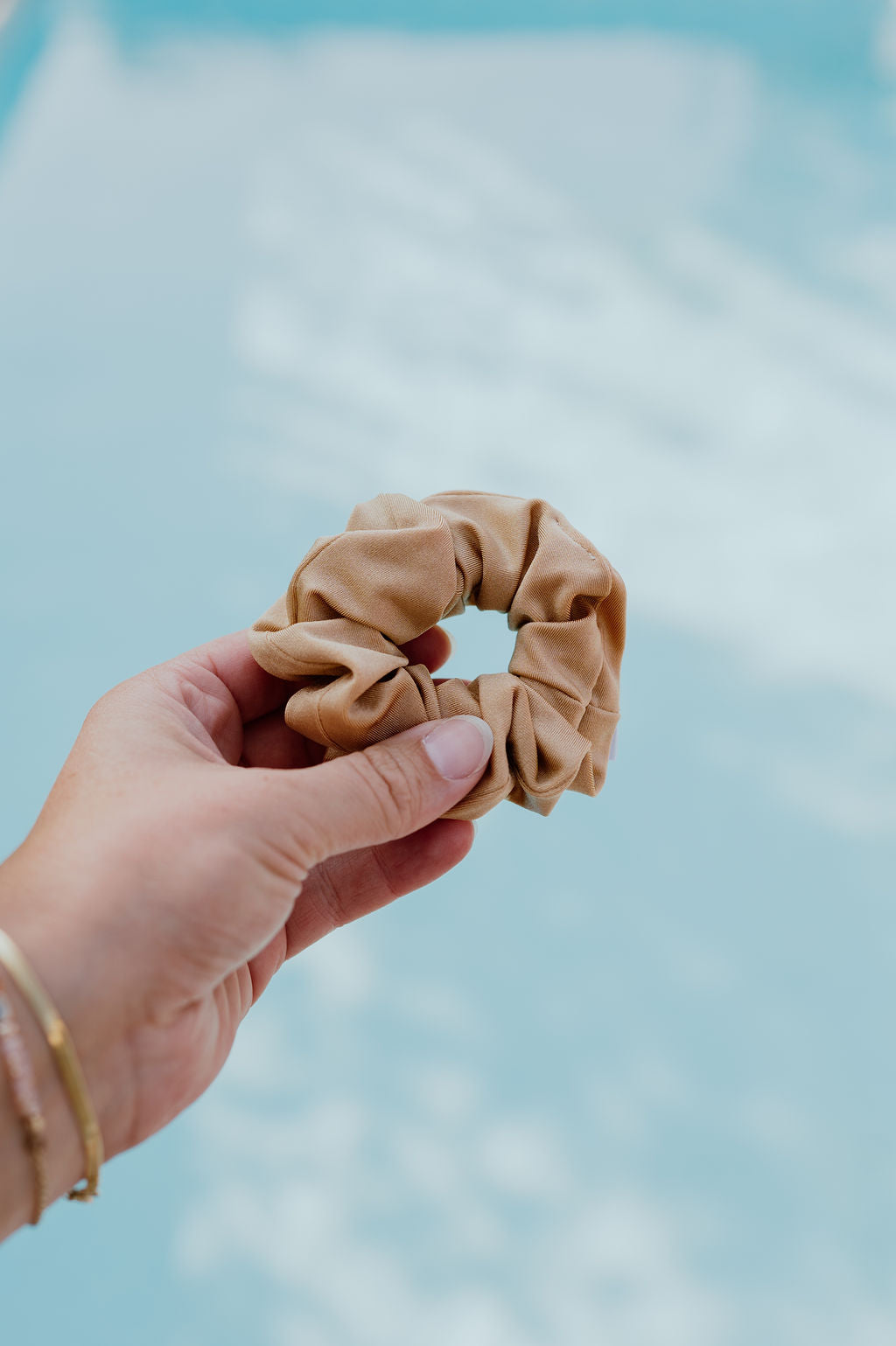 Hand holding a beige scrunchie against a blurred natural background
