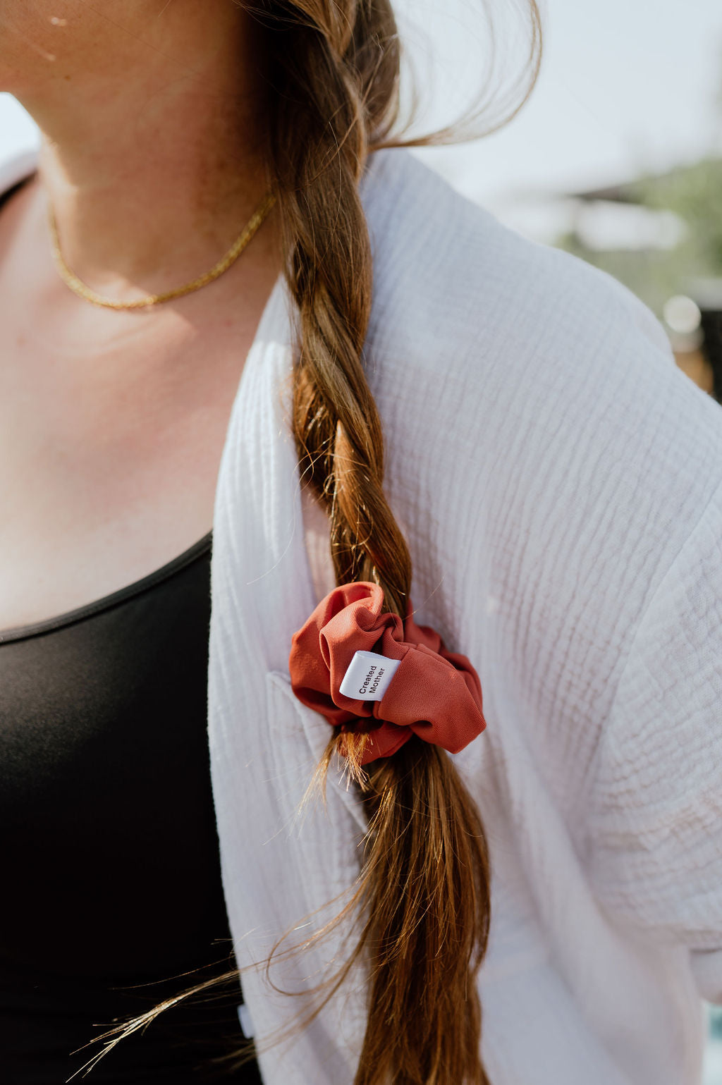 Person with braided hair wearing a deep orange scrunchie, blurred background