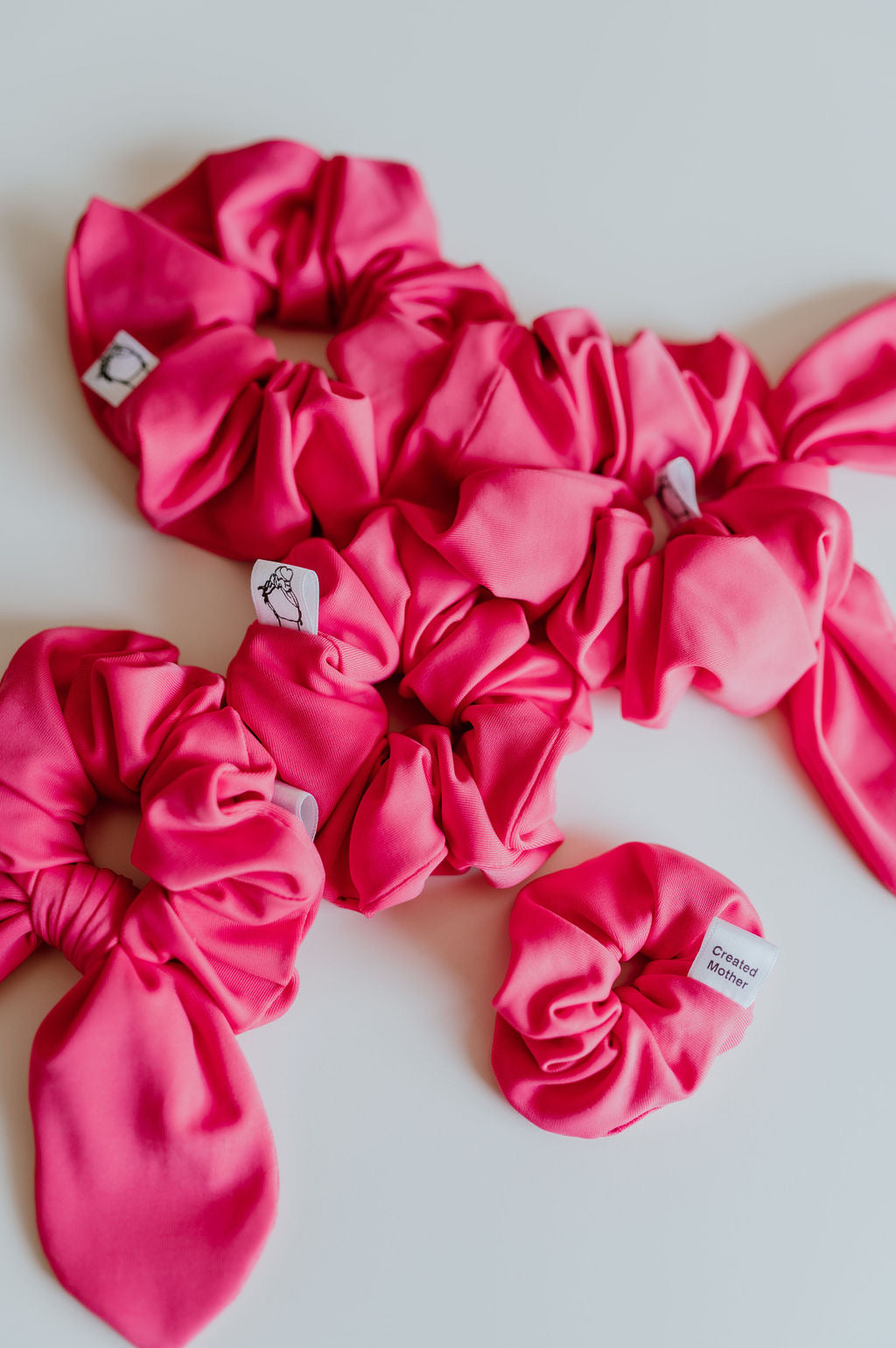Pink SWIM scrunchies with brand labels on a light gray background by Created Mother