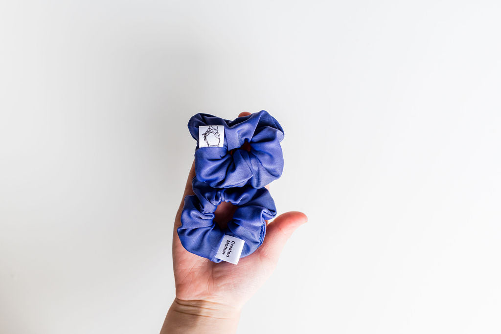 Hand holding two blue scrunchies against a white background