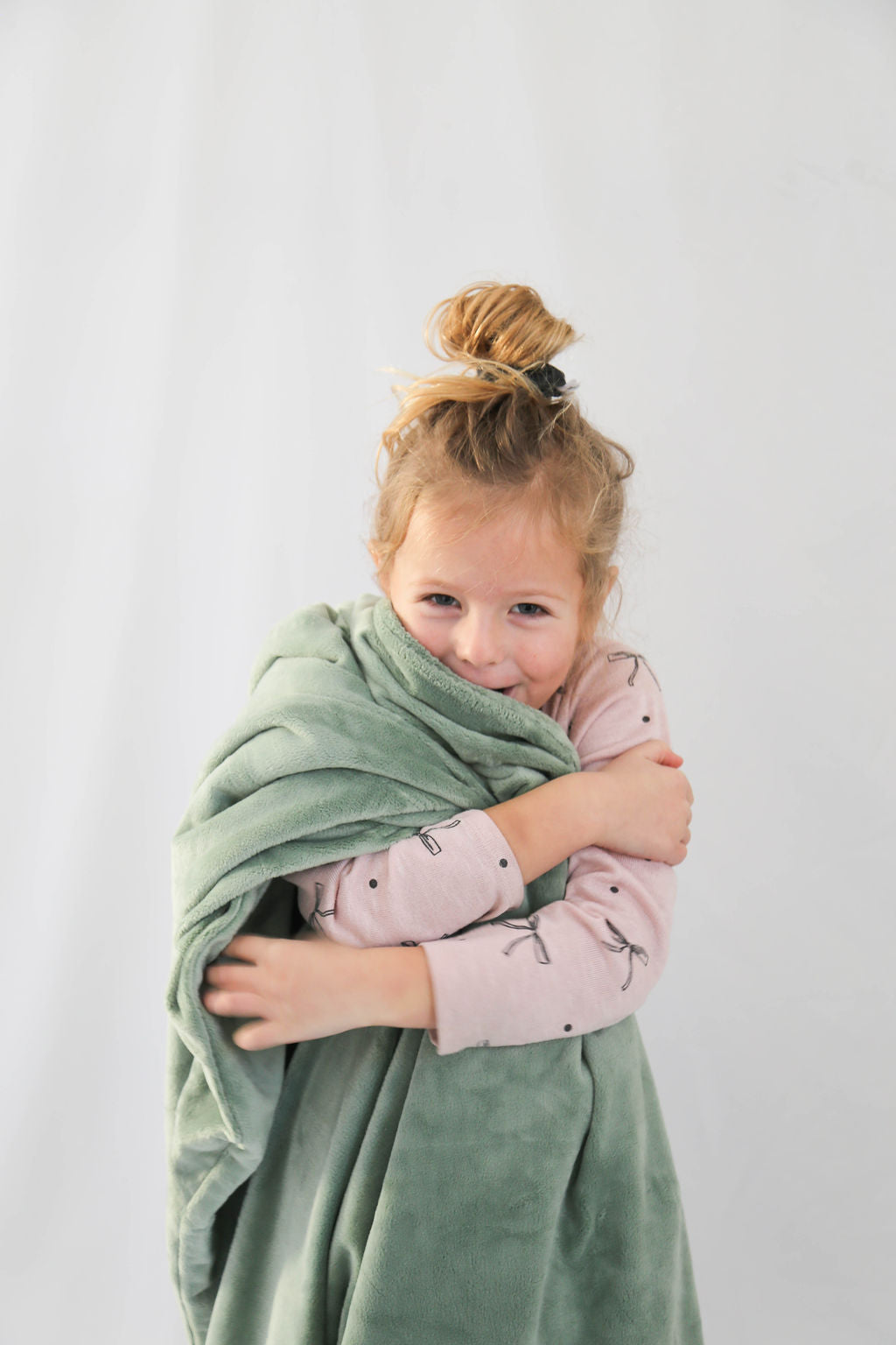 Child wrapped in a green blanket against a white background