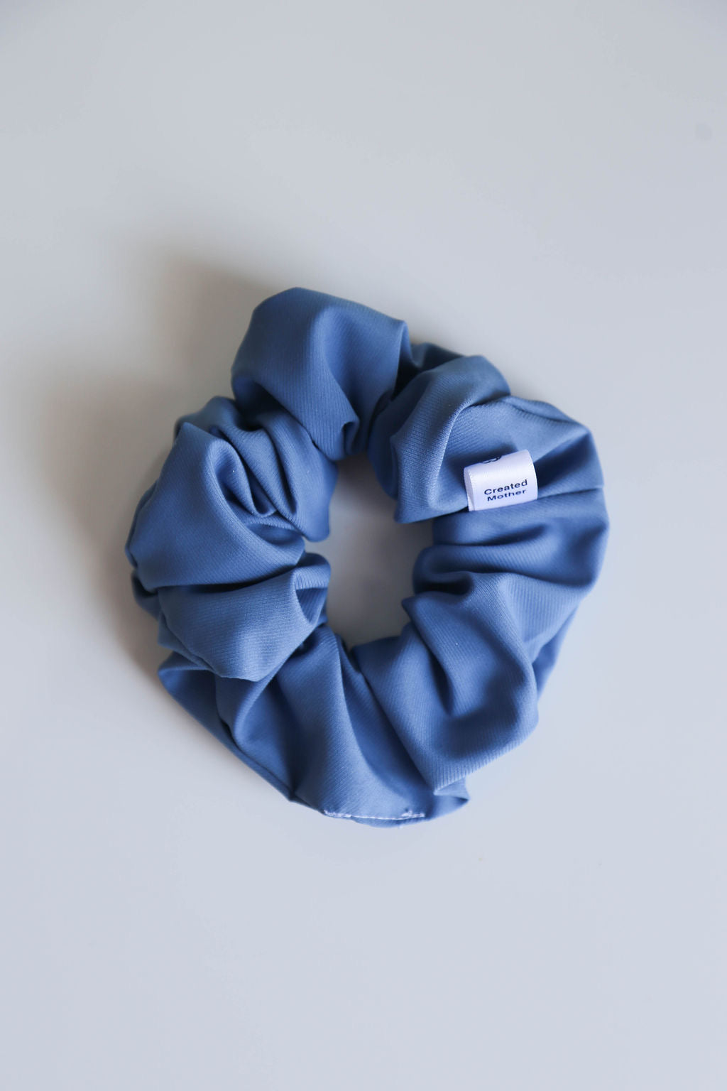 A handmade blue scrunchie crafted from medium-weight fabric with a subtle textured pattern.