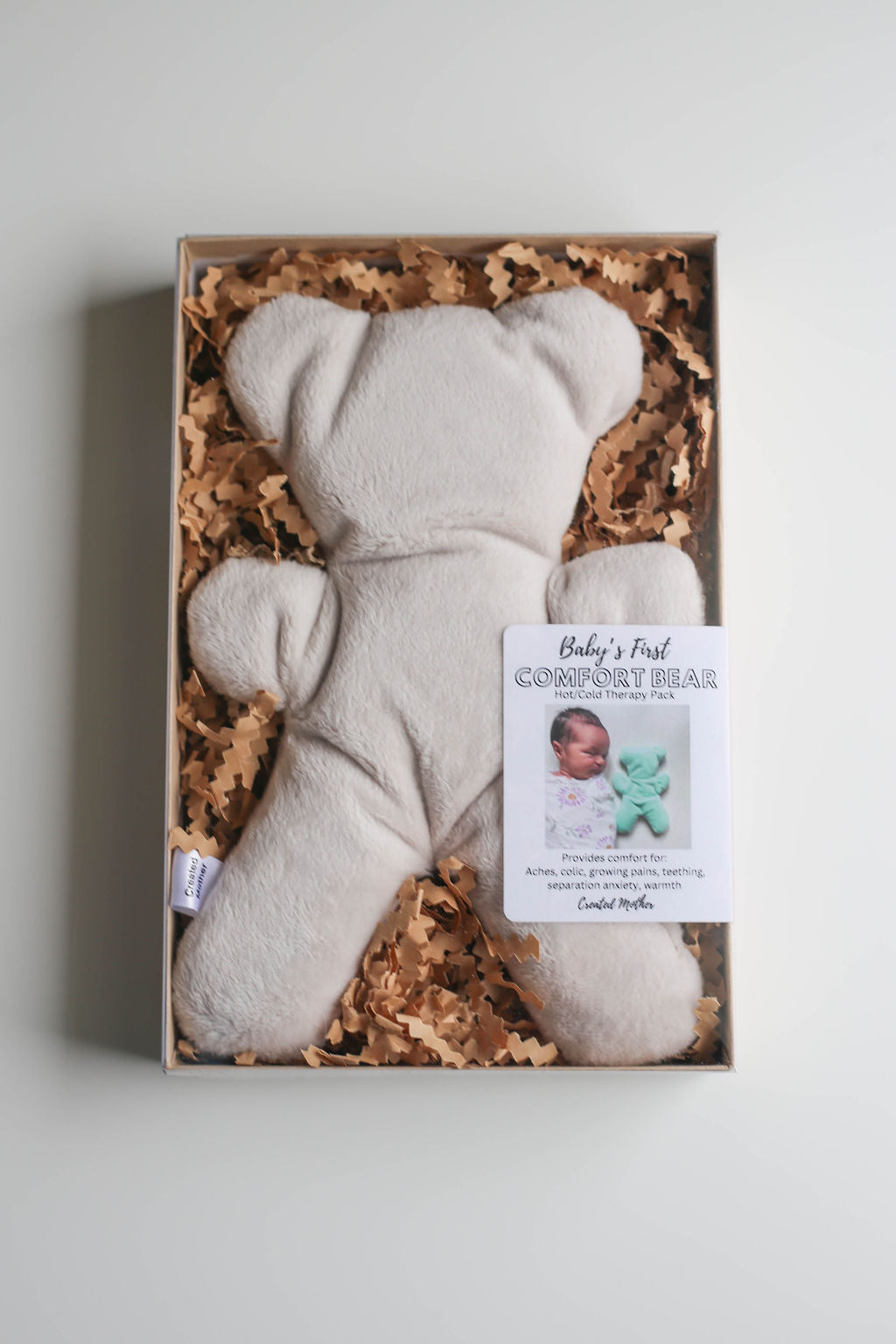Baby’s First Comfort Bear in neutral fabric, designed for soothing bumps, bruises, and colic.