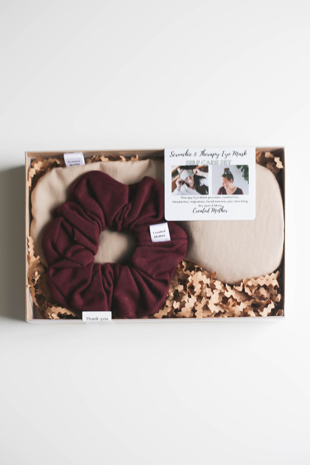 Neutral-colored hot/cold therapy eye mask and large classic scrunchie displayed in gift packaging.