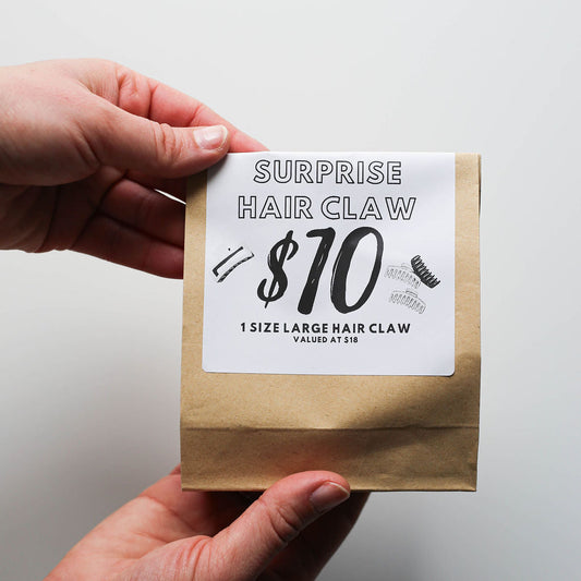 Hand holding a small kraft bag with a hair claw product and price label.