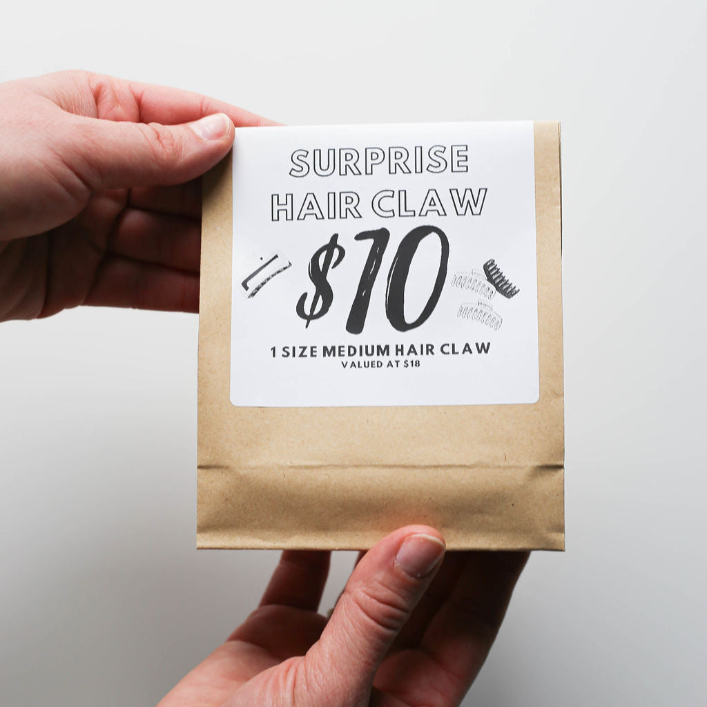 Hand holding a package with a label indicating a surprise hair claw product.