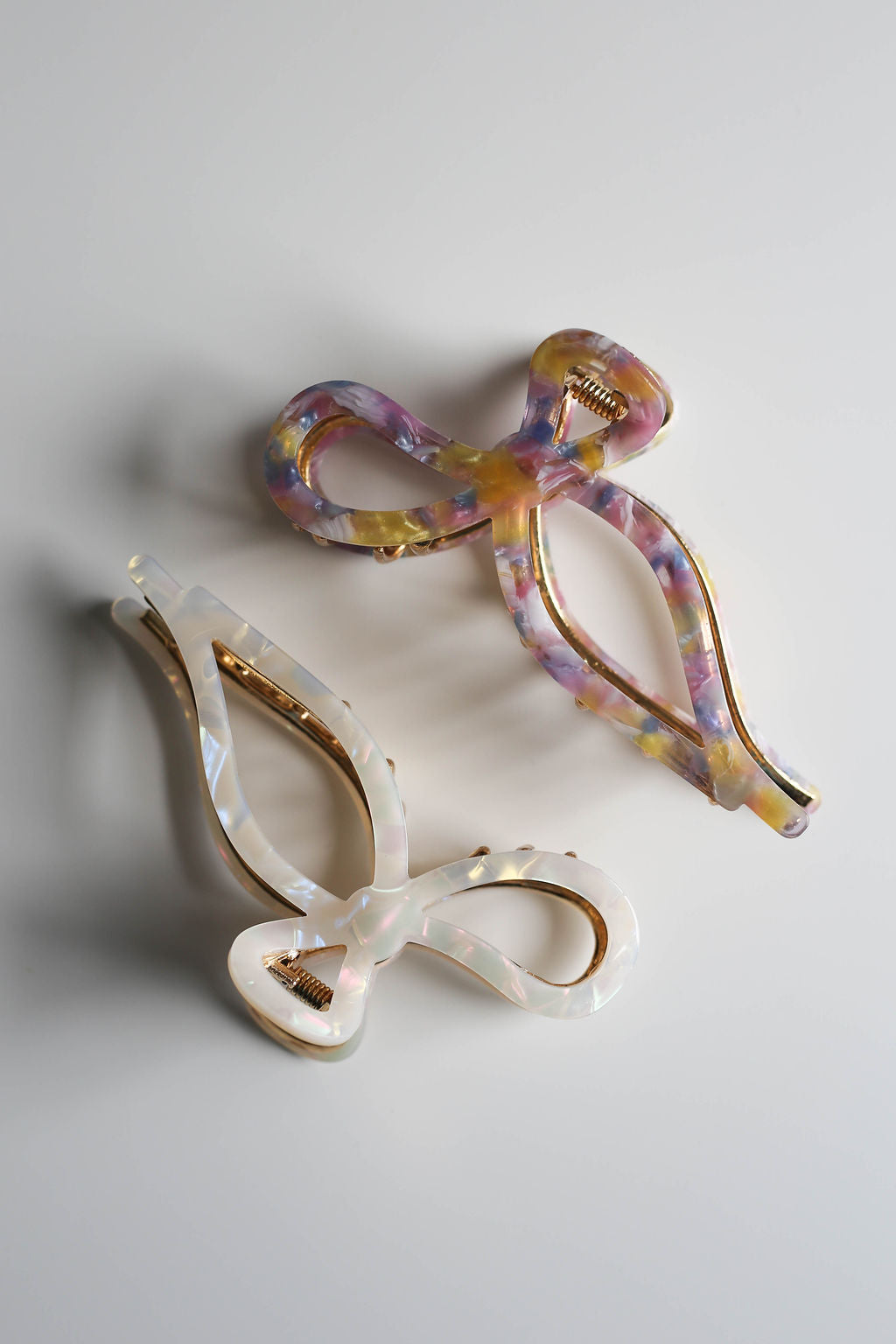 Stylish metal bow hair claw in white and gold, displayed on a white background.