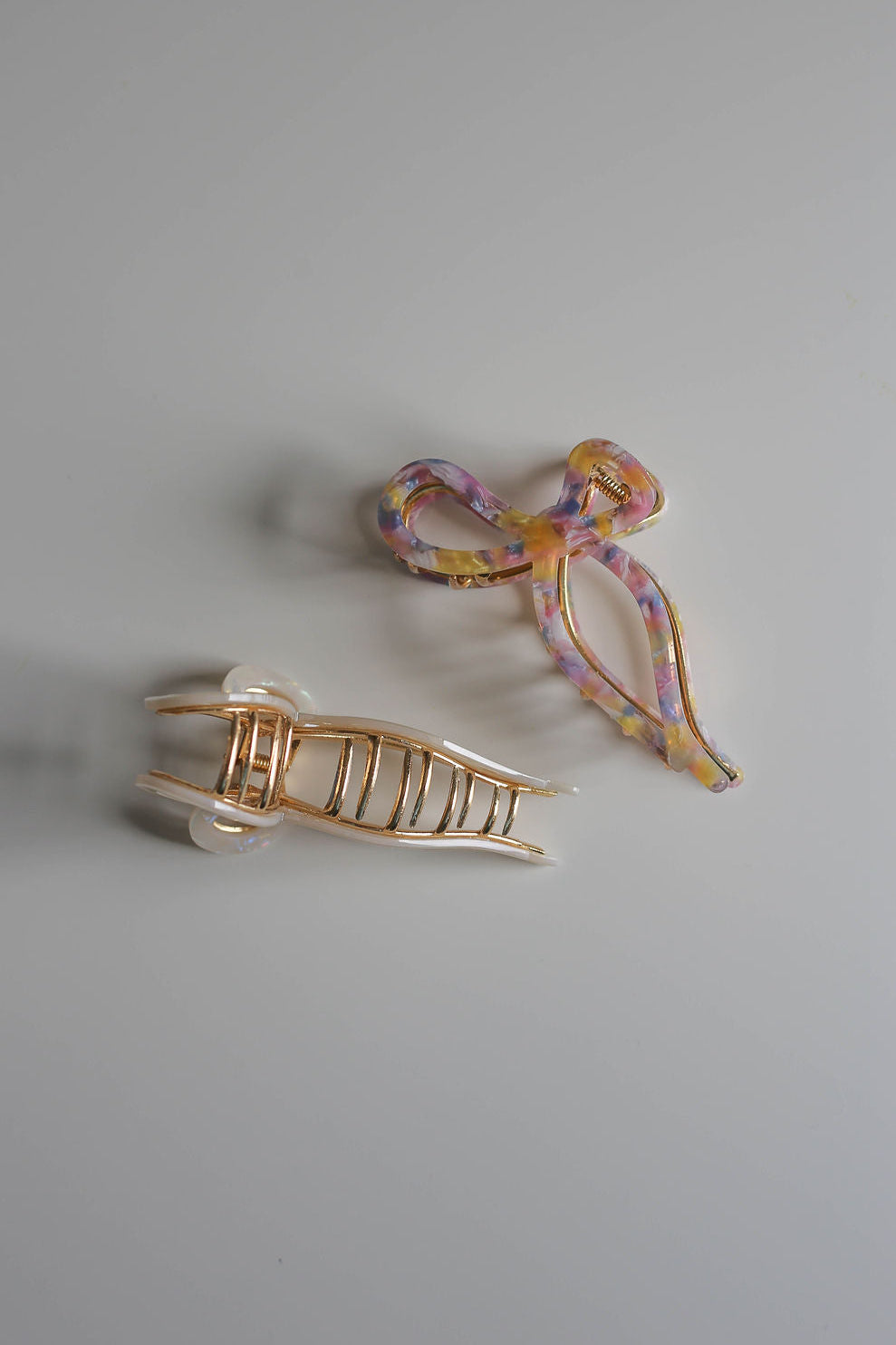 Two large bow hair claws—white opalescent and colorful purple—styled side-by-side.