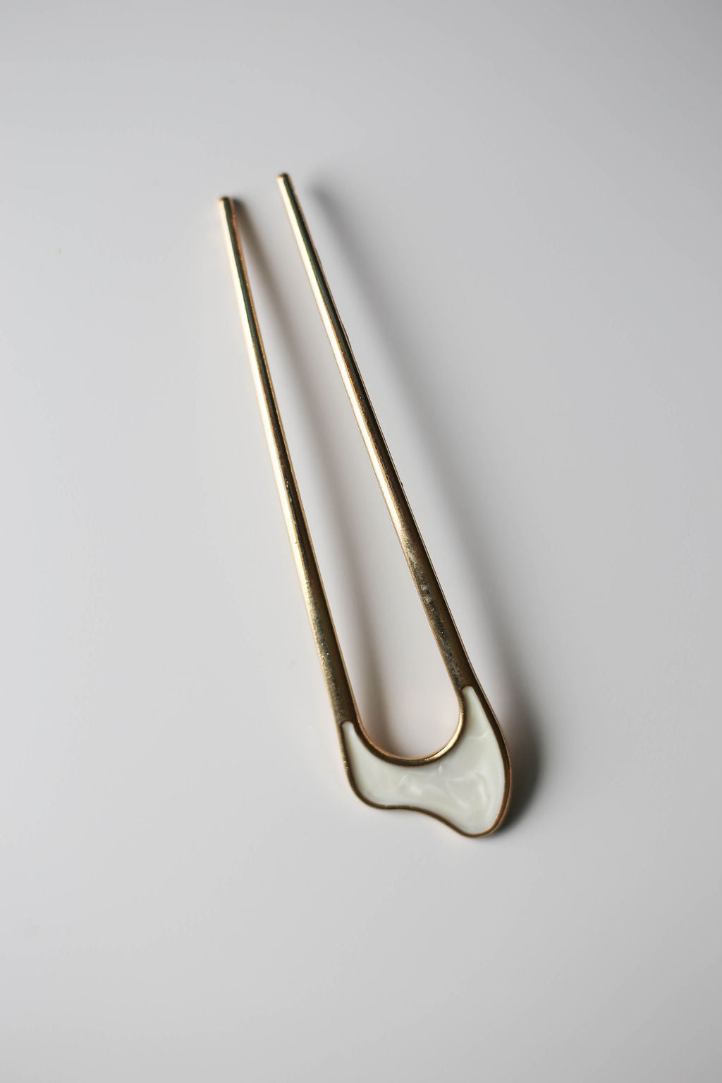 Chic metal pin for buns and twists, gold with white accent.