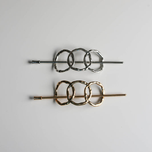 Two hair pins with interlocking circular designs on a light gray background
