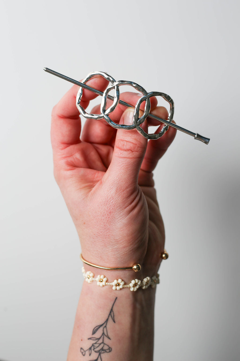 Hand holding a silver hairpin with interlocking rings against a plain background